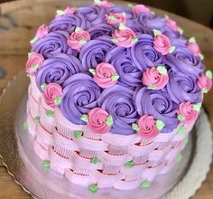 a cake with purple frosting and pink flowers sitting on top of a wooden table