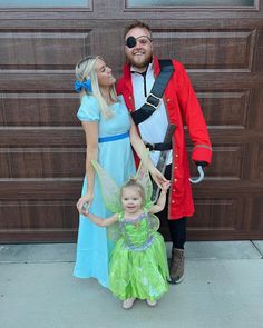 two adults and a child dressed up as peter pan and tinkerbell, standing in front of a garage door