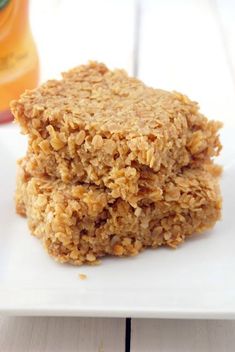 two oatmeal cookies on a white plate next to a bottle of orange juice