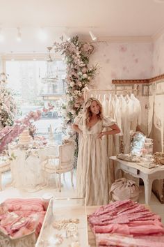 a woman standing in front of a dress shop with lots of dresses and accessories on display