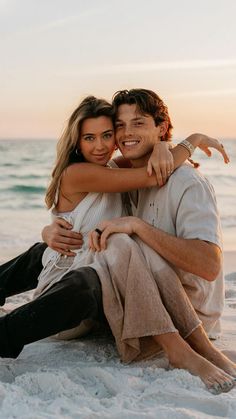 a man and woman sitting on the beach hugging each other with their arms around one another