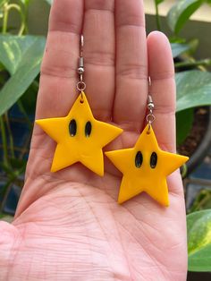 two yellow stars with black eyes are hanging from a persons hand in front of some plants