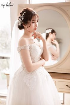 a woman in a white wedding dress looking at herself in the mirror with her hand on her cheek