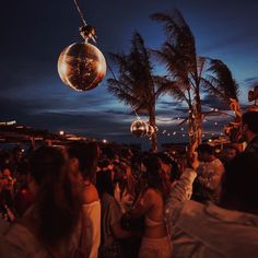 a group of people standing around with disco balls hanging from the ceiling and palm trees in the background