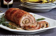 a large meatloaf roll on a plate next to some wine glasses and plates