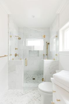 an all white bathroom with gold accents and marble flooring, along with a walk in shower