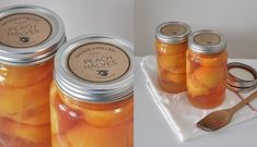 four jars filled with peaches sitting on top of a white tray next to a wooden spoon