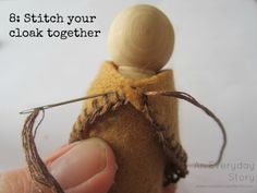 a hand holding a needle with a small wooden doll on it's back and the words, 8 stitch your cloak together