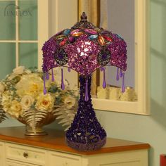 a purple lamp sitting on top of a wooden table next to a vase with flowers