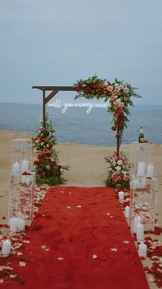 a red carpeted aisle with white candles and flowers on the ground next to an ocean