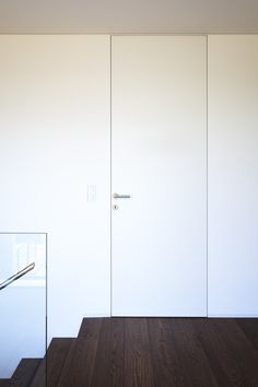 an empty room with wooden floors and white doors on the wall, next to a stair case