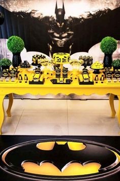 a yellow table topped with lots of cupcakes and batman decorations on top of it