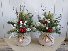 two vases with flowers and greenery are sitting on a burlap table