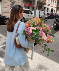 a woman is walking down the street with flowers in her hand and wearing a face mask