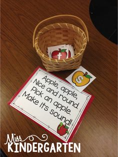 a basket with some cards and an apple in it sitting on a table next to a sign