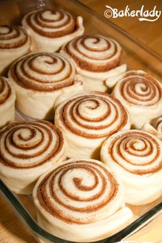 a glass dish filled with cinnamon rolls on top of a wooden table