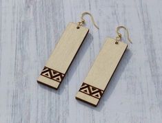 wooden earrings with geometric designs on them sitting on a white surface, against a blue background