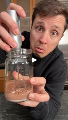 a man holding a glass jar with something in it and looking surprised at the camera