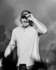 a black and white photo of a man holding his hat over his head while standing on stage