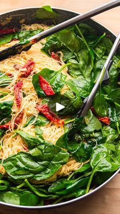 spinach and noodles are being cooked in a pan with tongs on the side