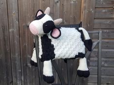 a crocheted cow sitting on top of a chair next to a wooden fence