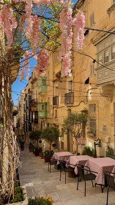 an alleyway with tables and chairs covered in pink tablecloths under blossoming trees