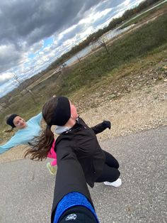 two girls are playing with a kite on the street in front of some water and clouds