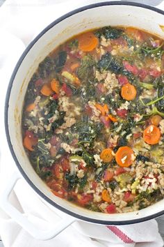 a pot filled with meat and vegetables on top of a white cloth next to a spoon