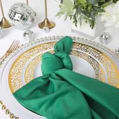 a place setting with green napkins and gold rimmed plates, silverware and flowers