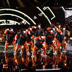 a group of people on stage with lights in the background and one person wearing an orange outfit