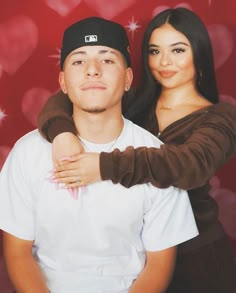 a young man and woman posing for a photo with hearts on the wall behind them