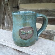 a green mug with a bow on it sitting on a ledge next to a wooden fence