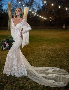 a woman in a wedding dress holding a bouquet and posing for the camera at night