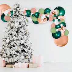 a decorated christmas tree in front of a white wall with balloons and presents under it