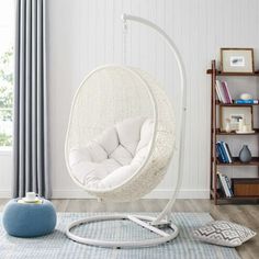 a white hanging chair in a living room next to a book shelf and blue rug