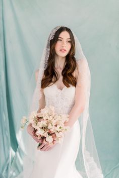 a woman in a white wedding dress holding a bouquet of flowers and wearing a veil