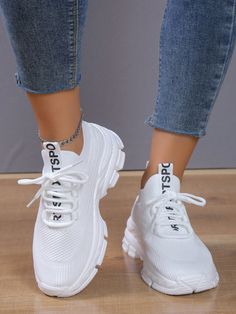 a woman wearing white sneakers and jeans standing on a wooden floor