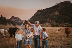 an adult and two children are standing in front of cows while the sun is setting