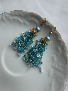 Discover the beauty of these handcrafted blue and gold seed bead earrings, accentuated with a sparkling zircon stone. Expertly made with attention to detail, these earrings offer a blend of elegance and charm, ideal for any occasion. The intricate design showcases vibrant colors that enhance their appeal, ensuring they complement both casual and formal attire with grace. Each pair is crafted uniquely, guaranteeing both quality and individuality. Treat yourself or a loved one to these exquisite earrings, perfect for adding a touch of sophistication to any outfit. Comes in a Cardboard box, ready to be a perfect gift for you or someone you want to make happy. P.S.   box, not the same as on the picture. Elegant Turquoise Earrings With Dangling Beads, Festive Turquoise Beaded Earrings, Turquoise Earrings With Gold Beads For Gift, Handmade Turquoise Crystal Earrings, Blue Earrings With Colorful Beads For Gift, Light Blue Beaded Dangle Earrings For Party, Festive Beaded Crystal Drop Earrings, Elegant Turquoise Beaded Earrings With Gold Beads, Blue Crystal Earrings With Faceted Beads As Gift