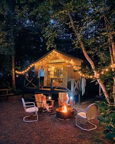 people sitting around a fire pit in front of a small cabin with lights on it