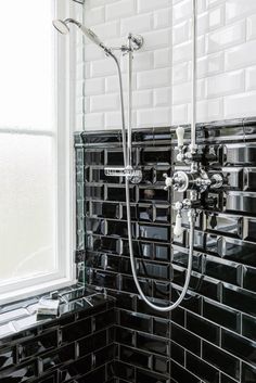 a black and white tiled bathroom with a shower head, handset, and window