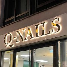 an illuminated sign that reads q - nails on the side of a building