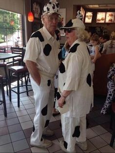 two older people dressed in costumes standing next to each other at a restaurant with tables and chairs