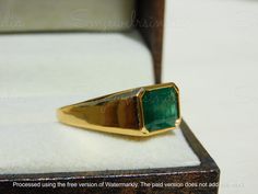 a gold ring with a green stone in it's center sitting on a white box