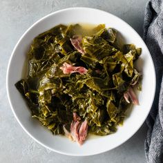 a white bowl filled with collard greens on top of a gray tablecloth next to a blue towel