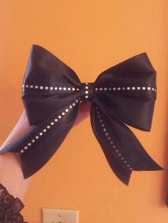 a woman's hand holding up a large black bow with pearls on the side