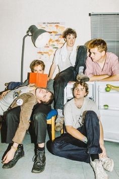 four young men sitting on the floor in front of a white refrigerator freezer and lamp