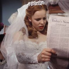 a woman in a wedding dress reading a newspaper while wearing a tiara and veil