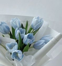 a bouquet of blue tulips is wrapped in white paper and held by a woman's hand