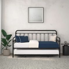 a black daybed with blue and white pillows in a room next to a potted plant